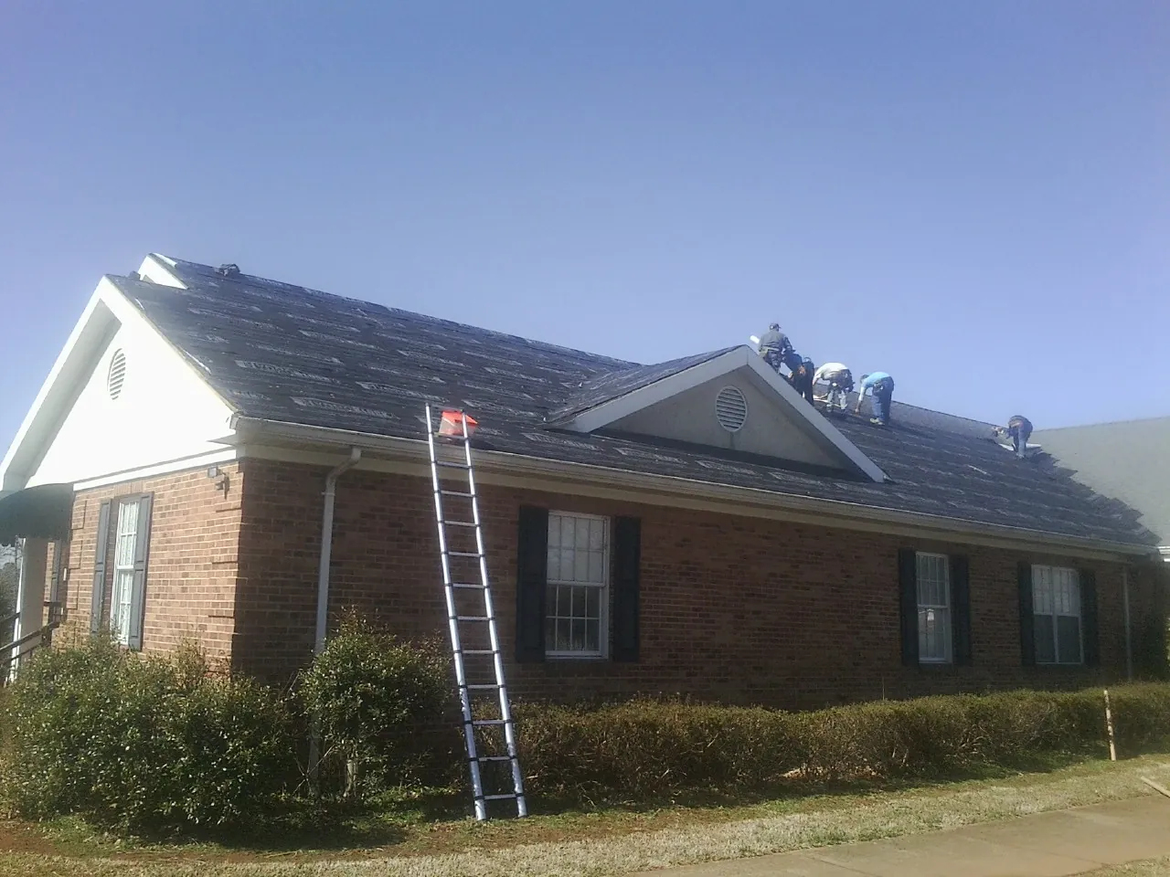 Crew tearing shingles off a brick ranch roof with a ladder set — Metal Roof Repair work by our crew in New Ringgold