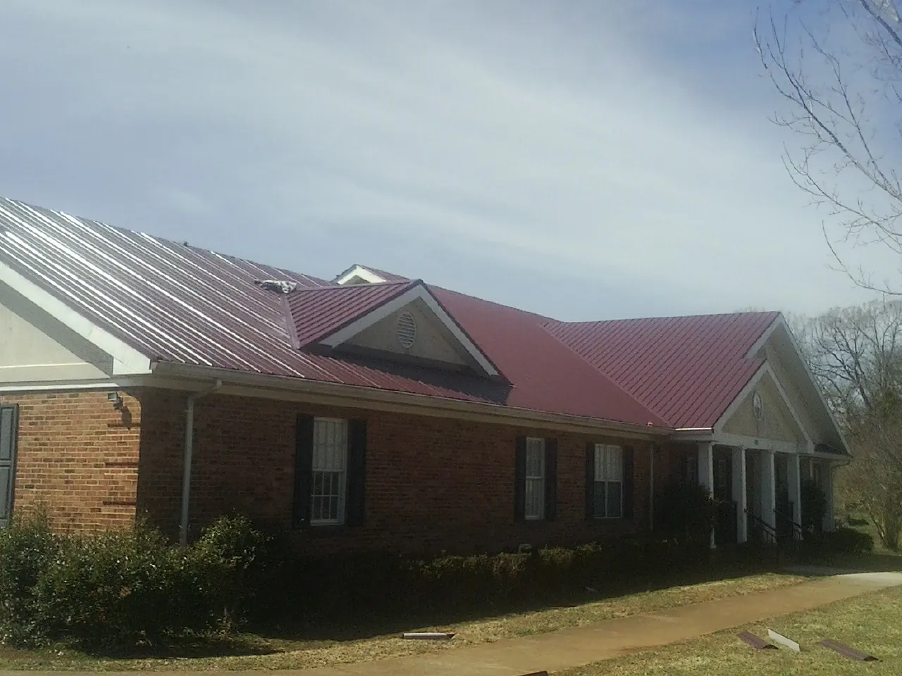 Red metal roof with gabled entries on a long brick building, from a Hail Damage Roof Repair job in New Ringgold