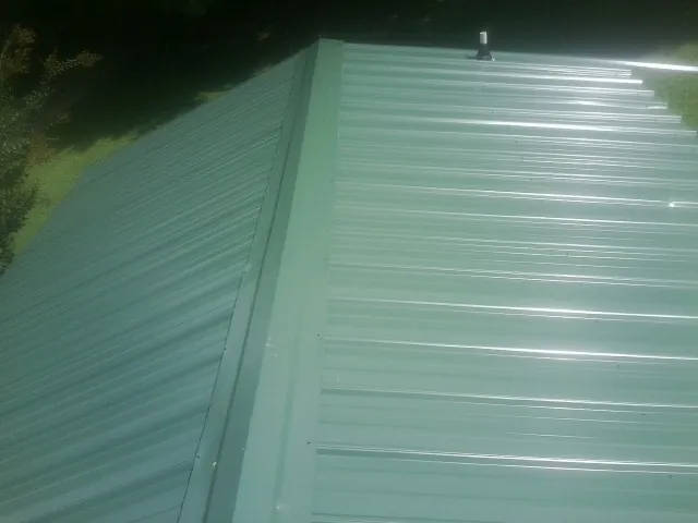 New green metal panels meeting at the ridge of a roof — Flat Roof Repair work by our crew in New Ringgold
