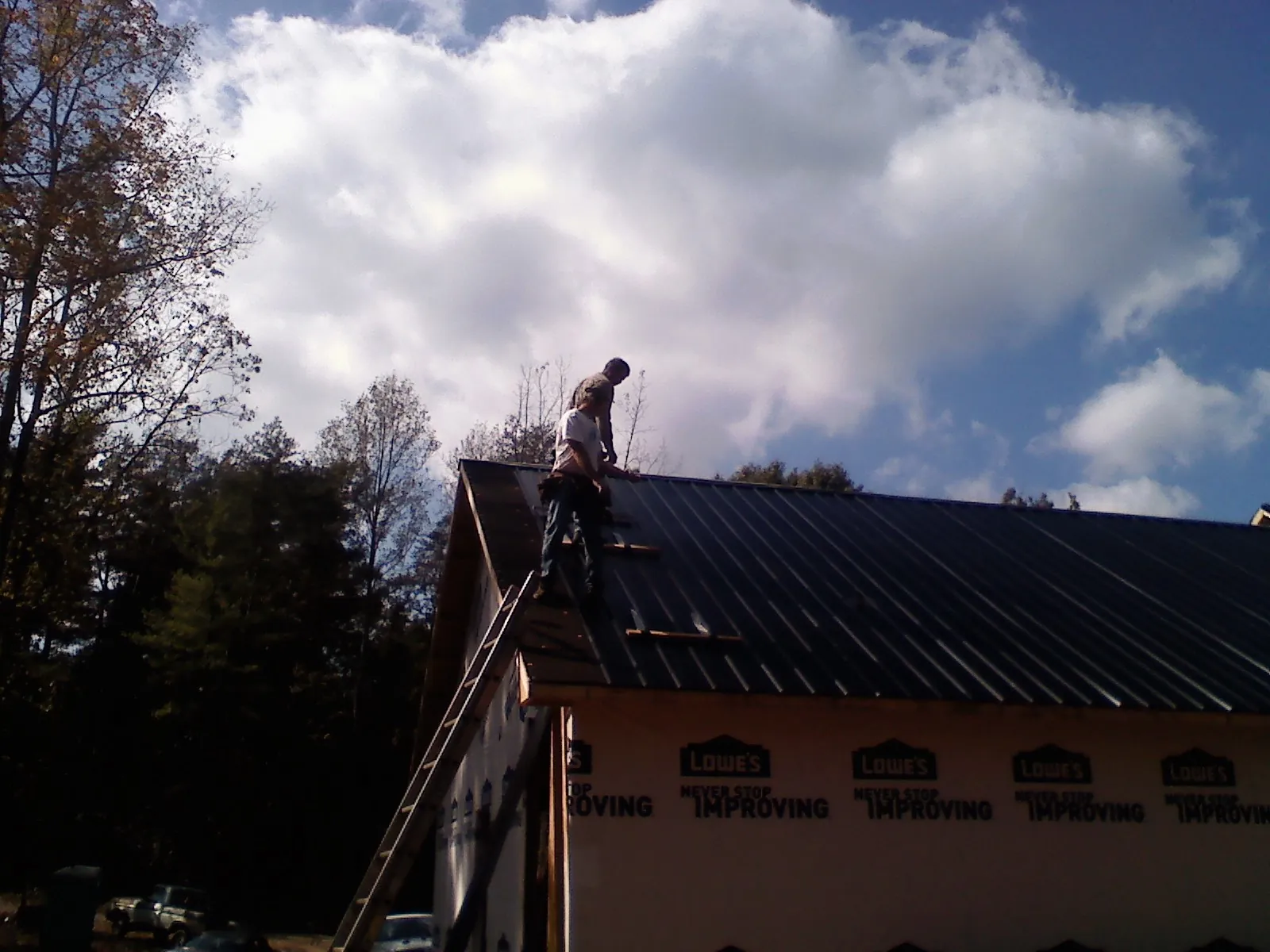 Roofer fastening dark metal panels high against a cloudy sky, from a Roof Inspection job in New Ringgold
