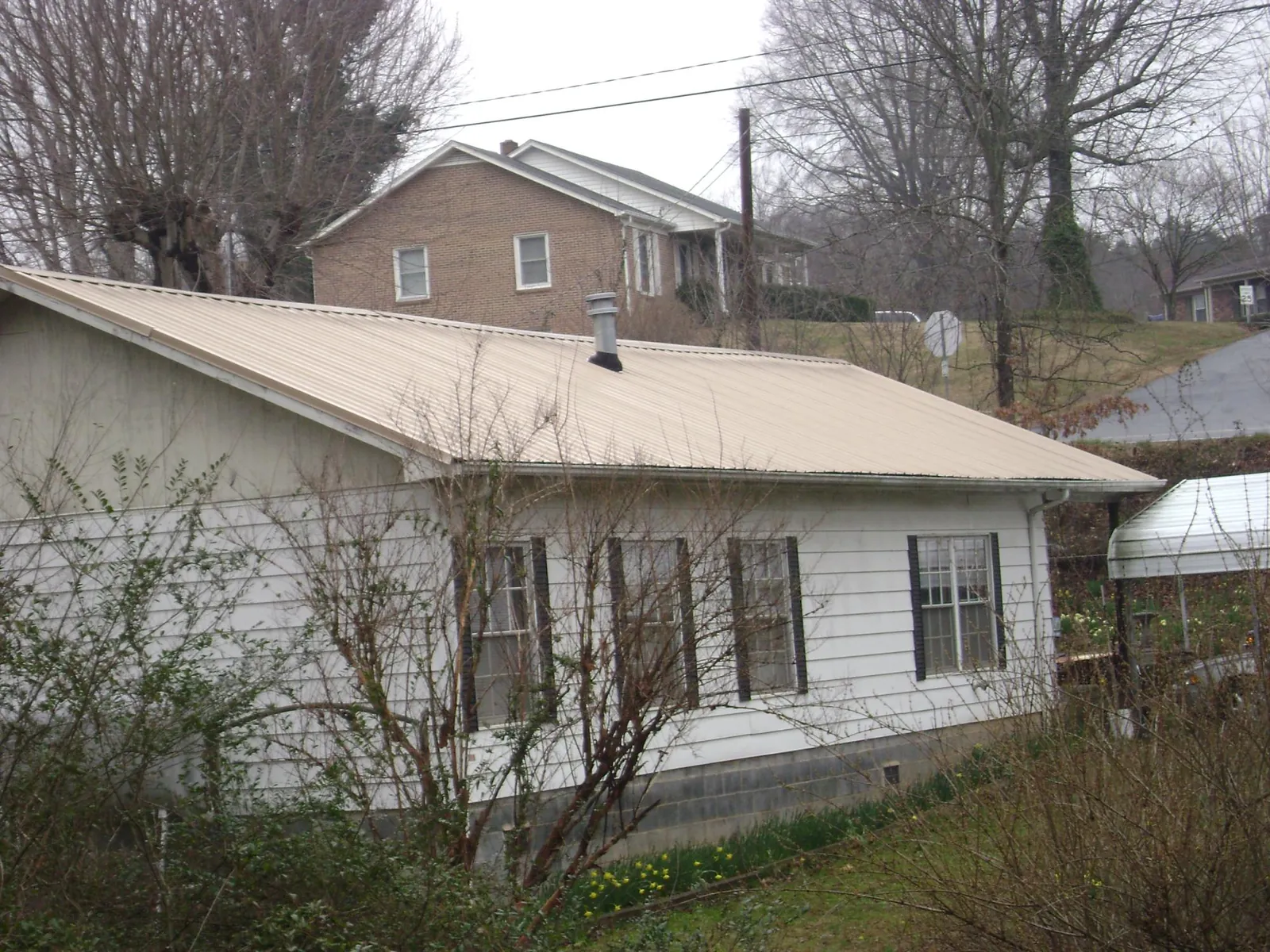 Tan metal roof on a white sided house set into a hillside — Commercial Roofing by Roofing Brothers in New Ringgold